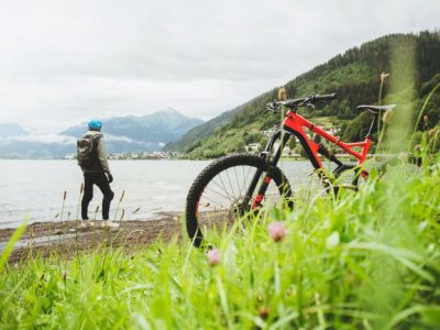 En strand med en röd mountainbike cykel och cyklisten på. Berg i bakgrunden.