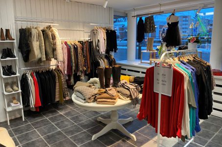 En klädbutik som säljer second hand-kläder. Till höger är en klädställning med vintage-skjortor i siden. På väggen hänger festklänningar och till vänster finns en hylla med skor.